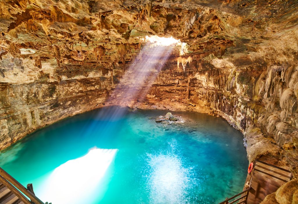 Een magische cenote in Yucatán, Mexico, met turquoise water, zonnestralen die door het gat in het plafond vallen en rotsformaties rondom.