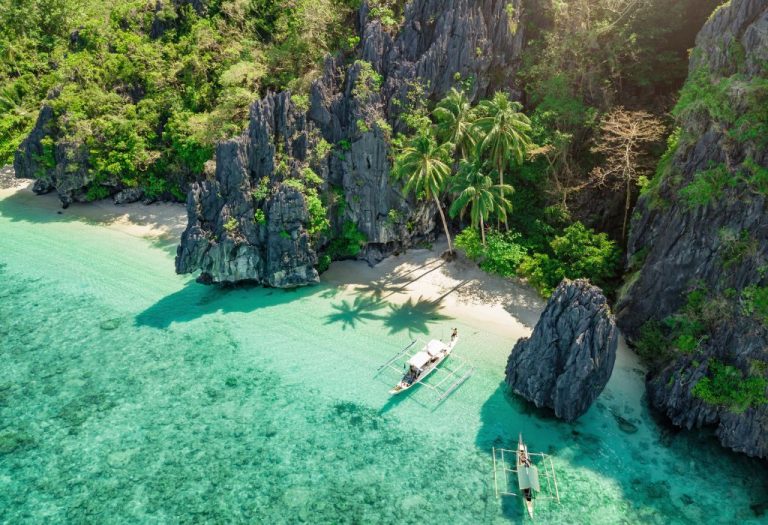 Tropische baai bij El Nido met turquoise water, kalkstenen rotsformaties, een rustige strandstrook en traditionele Filipijnse boten.